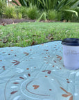 close up of a boho picnic rug corner with a coffee cup resting on it, on grass-Bilby Picnic Co